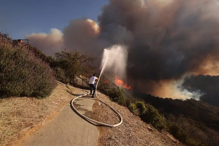 A-resident-attempts-to-protect-his-property-from-the-flames-closing-in-on-homes-threatened-by-the-wind-driven-Palisades-Fire-in-Pacific-Palisades-California-January-7-2025-A-fast-moving-brushfire-in-a-Los-Angeles-suburb-burned-buildings-and-sparked-evacuations-Tuesday-as-life-threatening-winds-whipped-the-region-More-than-200-acres-80-hectares-was-burning-in-Pacific-Palisades-a-upscale-spot-with-multi-million-dollar-homes-in-the-Santa-Monica-Mountains-shuttering-a-key-highway-and-blanketing-the-area-with-thick-smoke