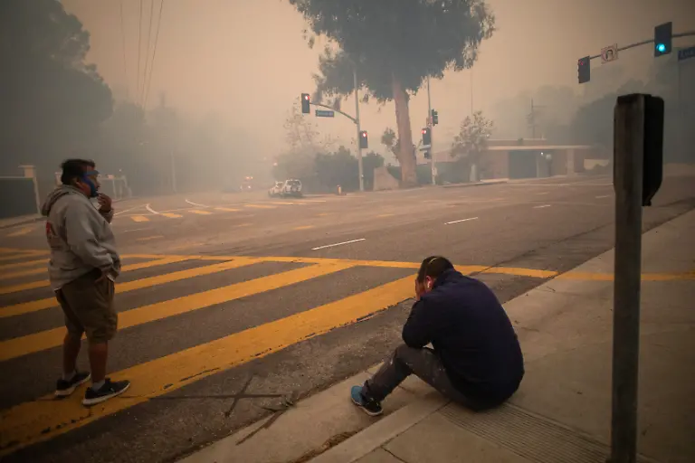 LOS-ANGELES-CALIFORNIA-JANUARY-7-People-stop-to-take-a-breath-as-they-evacuate-along-Sunset-Boulevard-while-the-Palisades-Fire-burns-amid-a-powerful-windstorm-on-January-7-2025-in-the-Pacific-Palisades-neighborhood-of-Los-Angeles-California-The-fast-moving-wildfire-is-threatening-homes-in-the-coastal-neighborhood-amid-intense-Santa-Ana-Winds-and-dry-conditions-in-Southern-California