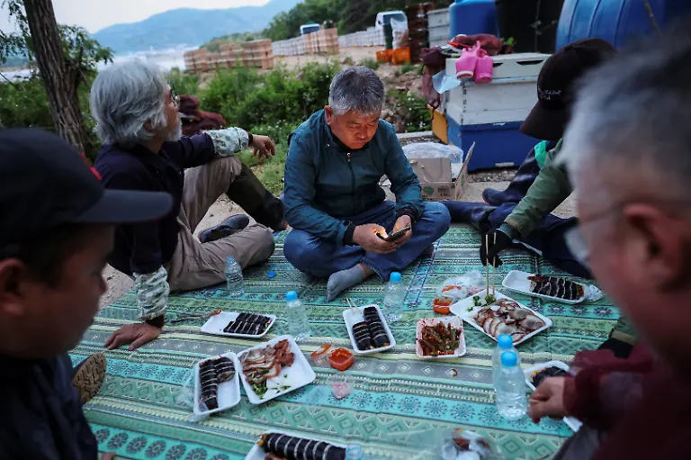 Park-Gyeong-je-65-a-migratory-beekeeper-and-his-workers-eat-dinner-while-preparing-to-move-hives-to-a-second-location-for-migratory-beekeeping-in-Gimcheon-South-Korea-May-12-2026-While-Park-used-to-make-four-trips-across-South-Korea-to-harvest-black-locust-honey-as-a-result-of-premature-blooming-he-now-makes-only-two-and-honey-production-takes-place-on-only-one-to-two-months-of-the-year-Compared-to-the-1990s-or-early-2000s-the-honey-harvest-has-decreased-by-about-70-percent-he-said-REUTERS-Kim-Hong-Ji-SEARCH-HONG-JI-SOUTH-KOREA-BEES-FOR-THIS-STORY-SEARCH-WIDER-IMAGE-FOR-ALL-STORIES