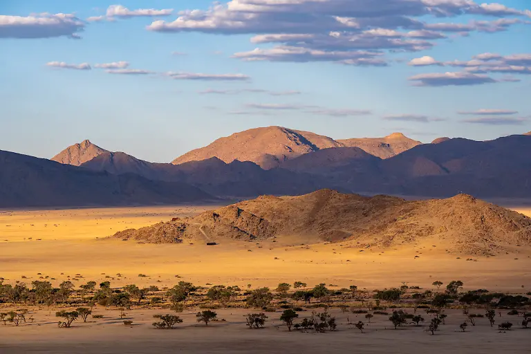 Wuestenlandschaft-mit-Bergen-im-Hintergrund-bei-Sonnenuntergang-nahe-Solitaire-Hardap-Namibia
