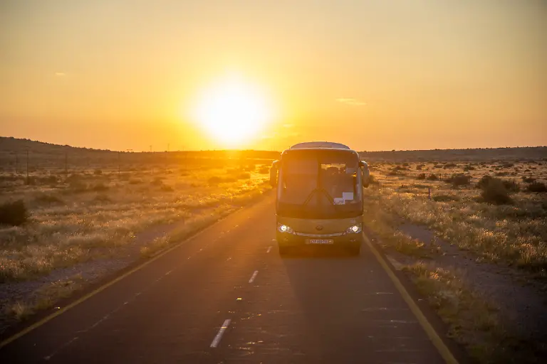 Reisebus-fuer-Passagiere-des-Boutique-Luxuszugs-African-Explorer-von-Rovos-Rail-Lernidee-Erlebnisreisen-auf-der-Strasse-bei-Sonnenaufgang-nahe-Upington-Nordkap-Suedafrika