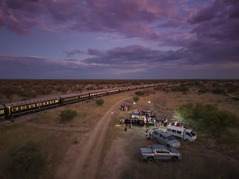 Luftaufnahmen-von-Passagieren-des-Boutique-Luxuszuges-African-Explorer-von-Rovos-Rail-Lernidee-Erlebnisreisen-beim-Geniessen-eines-Braai-Barbecue-Abendessens-in-der-Abenddaemmerung-Norman-Erongo-Namibia