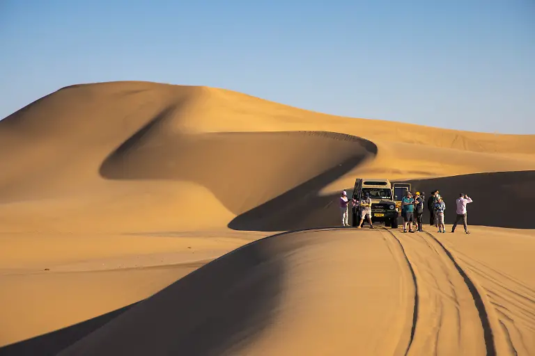 Menschen-stehen-auf-einer-Sandduene-neben-einem-Gelaendewagen-von-Little-Five-Desert-Safari-im-Dorob-Nationalpark-nahe-Swakopmund-Erongo-Namibia