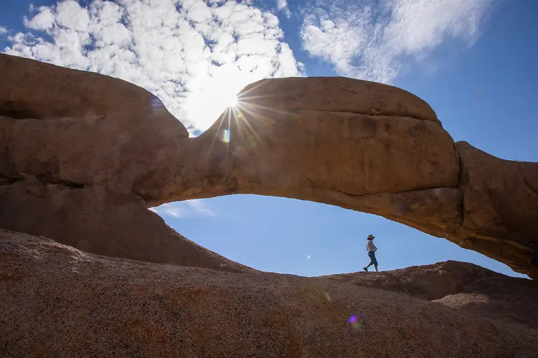 Silhouette-eines-Mannes-der-unter-einem-wunderschoenen-Steinbogen-im-Spitzkoppe-Naturschutzgebiet-Spitzkoppe-Erongo-Namibia-laeuft
