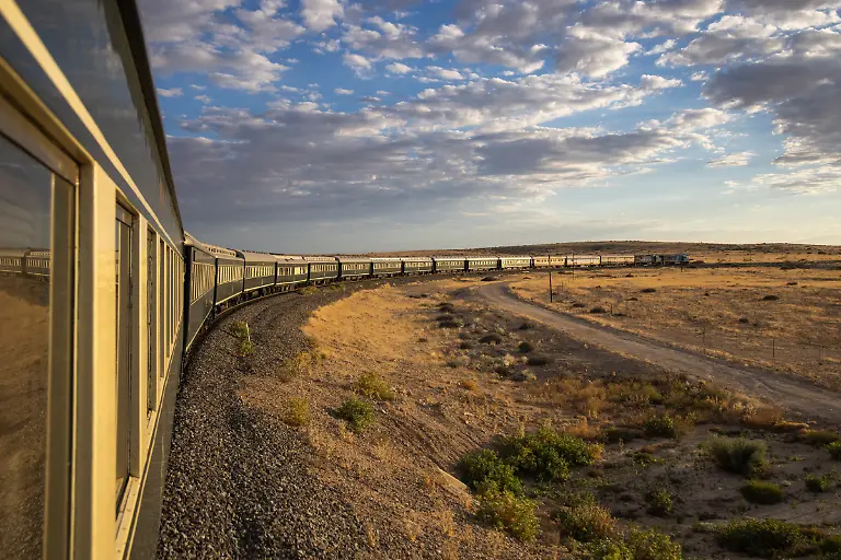 Seitenansicht-des-luxurioesen-Boutique-Zuges-African-Explorer-von-Rovos-Rail-Lernidee-Erlebnisreisen-auf-der-Fahrt-durch-eine-Wuestenlandschaft-bei-Sonnenaufgang-nahe-Usakos-Erongo-Namibia