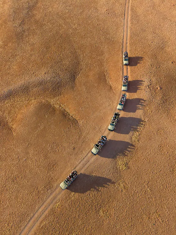 Luftaufnahme-von-Allrad-Safari-Fahrzeugen-der-Namib-Desert-Lodge-Gondwana-Collection-auf-einer-Schotterpiste-in-der-Wueste-nahe-Solitaire-Hardap-Namibia