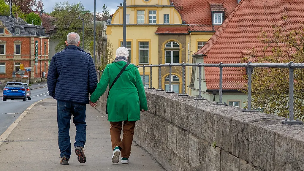 A-senior-couple-walks-hand-in-hand-on-a-bridge-in-Kitzingen-Lower-Franconia-Bavaria-Germany-on-April-19-2026-The-presence-of-older-residents-in-public-spaces-highlights-the-role-of-demographic-aging-retirement-and-pension-security-in-Germany-s-social-and-economic-planning