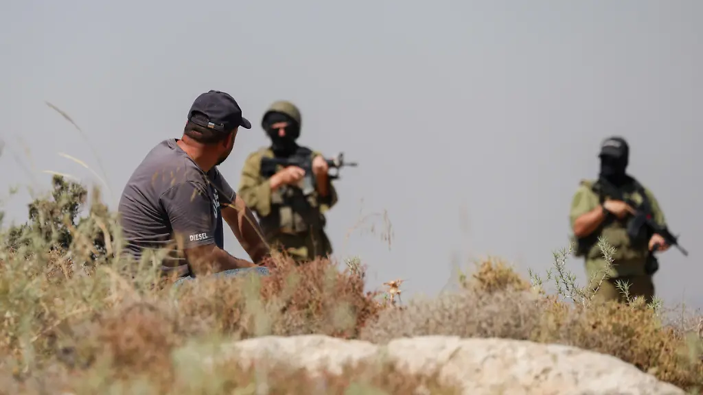 A-Palestinian-man-sits-on-a-rocky-hillside-as-Israeli-forces-stand-nearby-amid-smoke-near-Dura-southwest-of-Hebron-in-the-occupied-West-Bank-on-June-9-2026-Israeli-forces-dispersed-Palestinians-protesting-against-settlement-activity-near-Hebron-where-smoke-and-fires-were-seen-during-the-confrontation