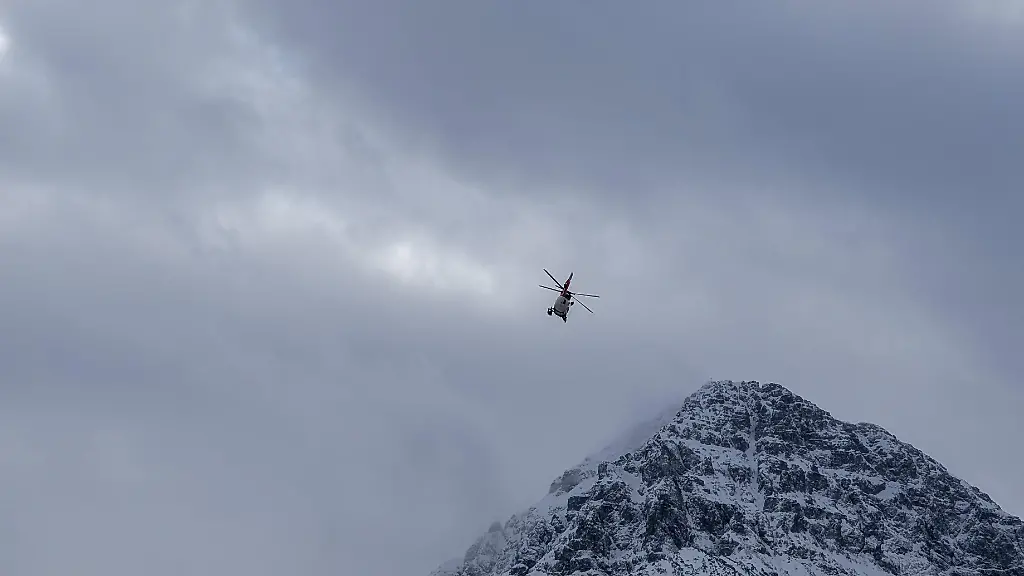 A-mountain-emergency-rescue-helicopter-flies-over-a-snow-covered-mountain-peak-in-Reutte-Tyrol-Austria-on-January-3-2026-The-state-of-the-art-red-and-white-aircraft-is-utilized-for-challenging-search-and-rescue-missions-in-the-alpine-terrain-of-the-greater-Reutte-area