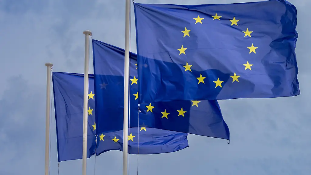 Drei-Flaggen-der-Europaeischen-Union-wehen-an-Fahnenmasten-vor-bewoelktem-Himmel-in-Strassburg-Die-Nahaufnahme-zeigt-das-EU-Symbol-mit-gelben-Sternen-auf-blauem-Grund-als-Motiv-fuer-Europapolitik-und-EU-Institutionen-EU-Flaggen-vor-bewoelktem-Himmel-Strassburg-28-04
