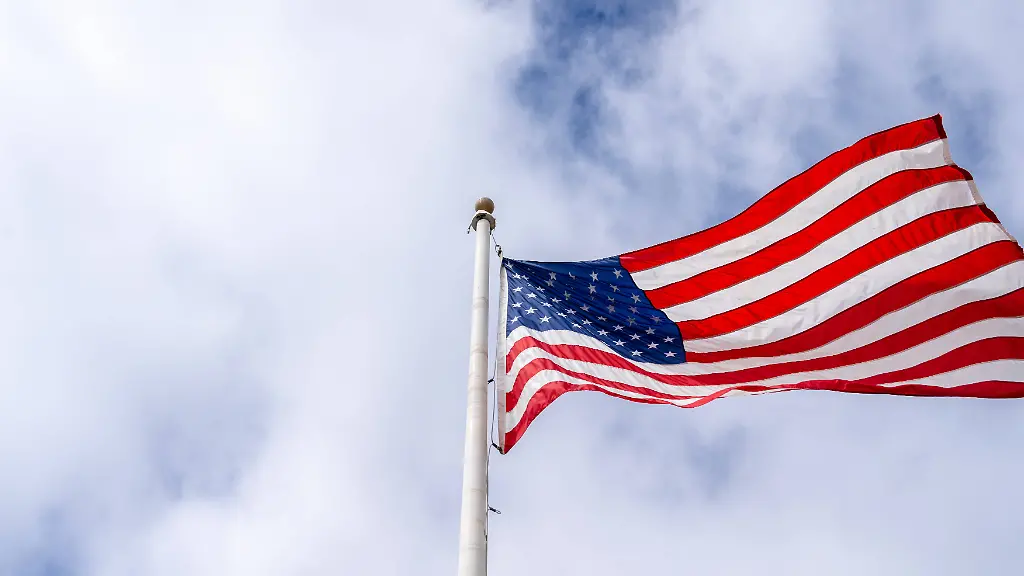 Eine-amerikanische-Flagge-weht-an-einem-hohen-Mast-vor-einem-bewoelkten-Himmel-The-United-States-flag-flutters-in-the-wind-displaying-its-red-white-and-blue-colors-with-stars-and-stripes-against-a-cloudy-background-LicenseRF-Copyright-xZoonar