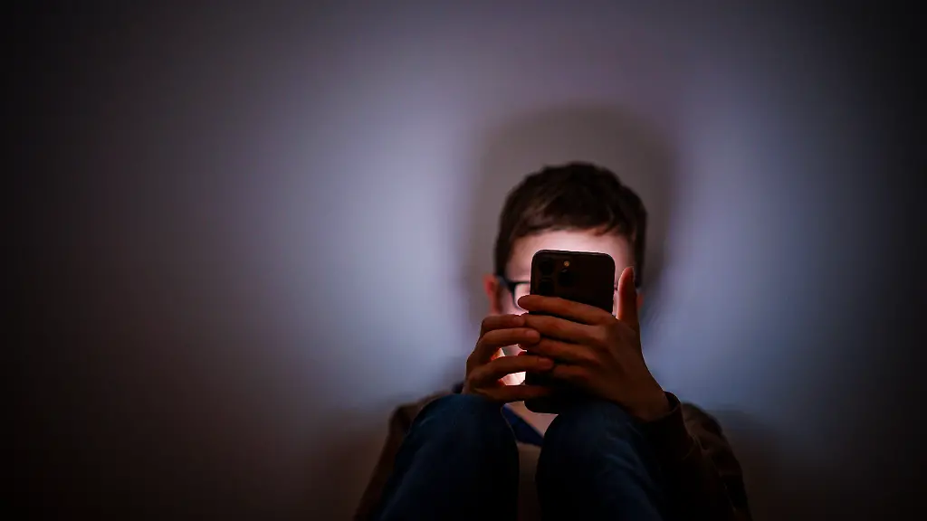 Symbolfoto-Gestellte-Aufnahme-zum-Thema-Kinder-nutzen-Social-Media-Ein-Junge-sitzt-in-einem-dunklen-Raum-und-wird-von-einem-Smartphone-beleuchtet-Berlin-16-02-2026