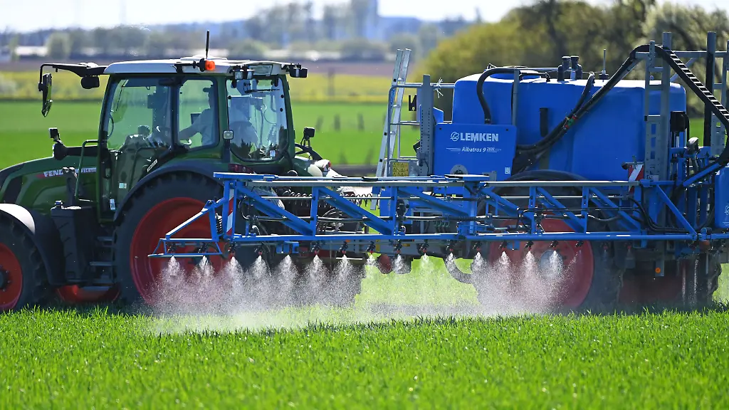 Themenfoto-Landwirtschaft-Duengen-Ein-Landwirt-faehrt-mit-seinem-Traktor-und-einer-Anhaengerfeldspritze-ueber-ein-Feld-mit-Jungpflanzen-und-duengt-mit-Fluessigduenger-Duengemittel