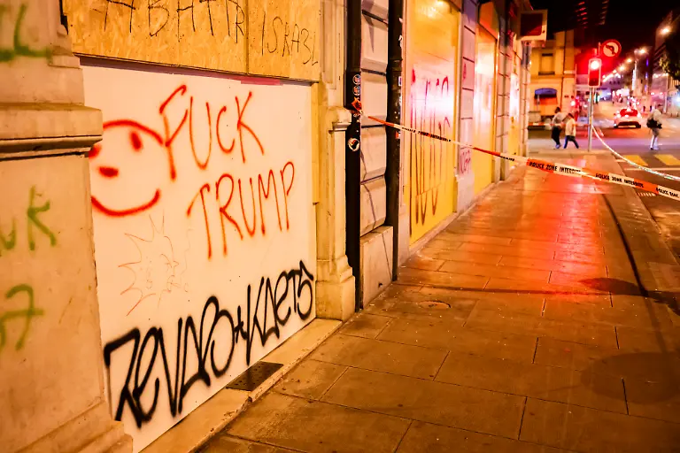 Eine-Person-geht-nachts-an-mit-Fuck-Trump-Graffiti-beschmierten-Holzpaneelen-vorbei-die-zum-Schutz-der-Fassade-waehrend-einer-Demonstration-gegen-den-G7-Gipfel-angebracht-wurden