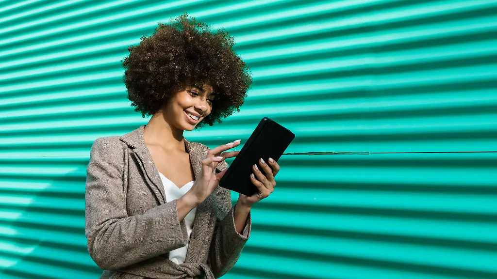 Smiling-woman-browsing-tablet-outdoors-by-a-turquoise-wall-model-released-Symbolfoto-EGAF02621
