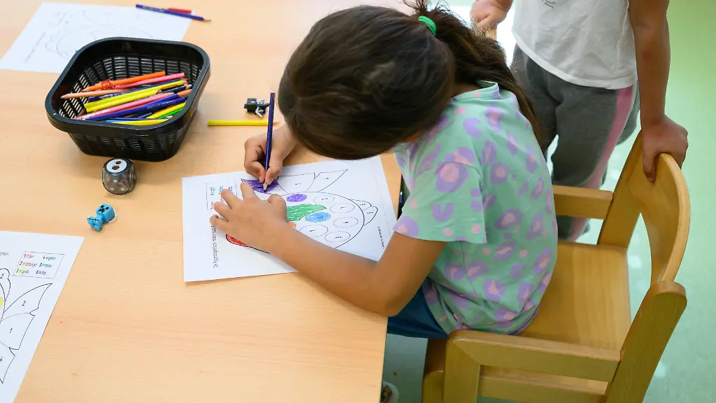 Ein-Maedchen-aus-einer-Fluechtlingsfamilie-sitzt-an-einem-Tisch-und-malt-im-Kindergarten-des-Chancencenters-der-Landesuebergangseinrichtung-Das-Chancencenter-soll-Menschen-mit-unsicherem-Aufenthaltsstatus-aufnehmen-die-aus-objektiven-Gruenden-nicht-abgeschoben-werden-koennen-Nach-einer-Testphase-beginnt-dort-nun-der-Regelbetrieb