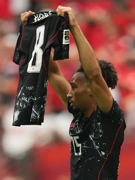 Fussball-Maenner-WM-2026-Kanada-Katar-Vorrunde-Gruppe-B-2-Spieltag-BC-Place-Vancouver-Der-Kanadier-Nathan-Saliba-haelt-nach-seinem-Tor-zum-4-0-das-Trikot-von-Ismael-Kone-hoch-Kone-hatte-sich-im-Spiel-verletzt-und-musste-vom-Feld-getragen-werden