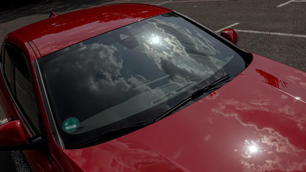 Ein-erneut-sehr-heisser-heisser-Tag-im-Siegerland-Das-Sommerwetter-geht-weiter-Ein-rotes-Auto-steht-in-der-Sonne-auf-einem-Parkplatz-und-heizt-sich-auf-Die-Sonne-und-Wolken-spiegeln-sich-in-der-Frontscheibe-und-am-Fahrzeuglack-Wer-bei-diesen-Temperaturen-ein-Kind-oder-Hund-im-Fahrzeug-zuruecklaesst-zuruecklaesst-handelt-verantwortungslos-Symbolbild-erhitztes-Auto-am-14-08-2025-in-Siegen-Deutschland