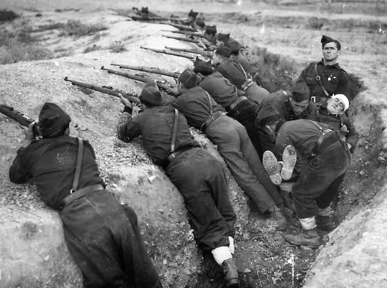 Schuetzengraben-der-Aufstaendischen-in-Guadarrama-bei-der-Schlacht-um-Madrid-Die-Soldaten-sind-mit-ihren-Gewehren-positioniert-waehrend-ein-Verwundeter-weggetragen-wird-Spanien-Photographie