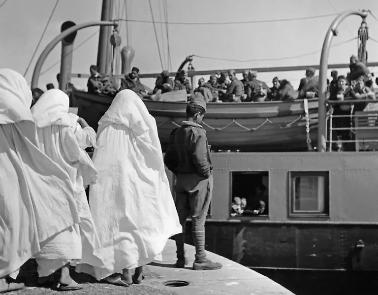 Aufnahme-von-marokkanischen-Soldaten-der-spanischen-Fremdenlegion-beim-Ausschiffen-ais-dem-Hafen-von-Tetouan-Spanisch-Marokko-aufs-spanische-Festland-Im-Vordergrund-verabschieden-verschleiderte-Frauen-die-Maenner-Die-Aufstaendischen-verlegten-Tausende-marokkanischer-Soldaten-fuer-den-Kampf-auf-nationalspanischer-Seite-aus-Marokko-nach-Spanien-Aufnahmedatum-18-07-1936-31-07
