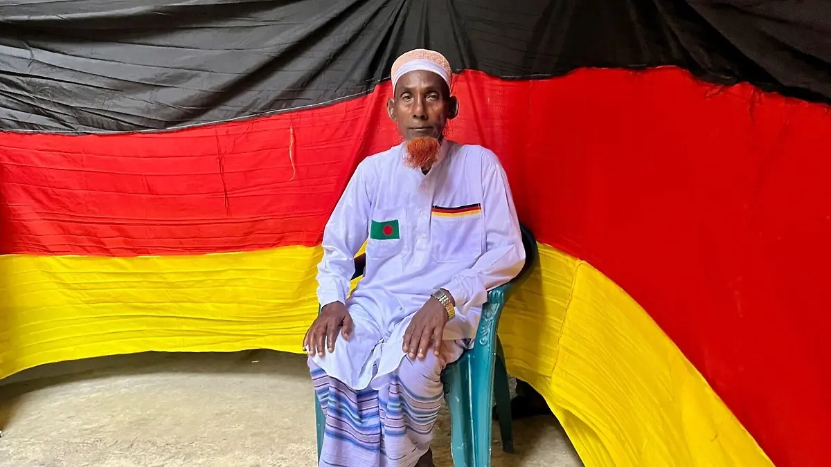 Der-77-jaehrige-bangladeschische-Bauer-Amjad-Hossain-posiert-mit-der-deutschen-Flagge-die-er-zu-Hause-genaeht-hat-Er-entrollte-die-7-5-Kilometer-lange-Flagge-am-10-Juni-auf-dem-Pausenplatz-einer-oertlichen-Schule-einen-Tag-vor-Beginn-der-FIFA-Weltmeisterschaft-2026