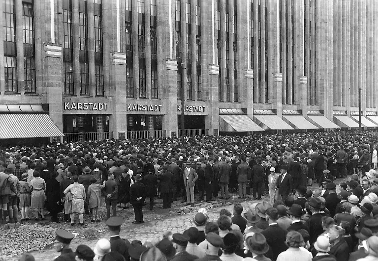 GERMANY-BERLIN-1929-06-21-Original-caption-DIE-EROeFFNUNG-VON-BERLIN-S-GROeSSTEM-WARENHAUS-On-Friday-the-21st-of-June-the-Riesenbau-des-neuen-Karstadt-Geschaeftshauses-opened-in-Berlin-Neukoelln-the-biggest-warehouse-in-Germany-maybe-even-in-Europe-Unsere-Aufnahme-zeigt-die-gewaltigen-Menschenmassen-die-sich-vor-dem-Riesenbau-am-Eroeffnungstage-eingefunden-hatten-und-nur-von-einem-grossen-Polizei-aufgebot-zur-Freihaltung-der-Verkehrsstrassen-werden-behalten-werden