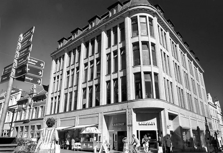 Touristen-und-Einwohner-der-Stadt-laufen-am-Mittwoch-28-07-1999-am-Stammhaus-der-Karstadt-AG-in-Wismar-vorbei-Rudolph-Karstadt-war-im-Mai-1881-mit-einem-Moebelwagen-voller-Stoffe-in-die-Hansestadt-gekommen-und-begann-den-Handel-mit-festen-Preiskalkulationen-Am-Freitag-30-07-1999-stimmen-die-Karstadt-Aktionaere-ueber-die-einschneidende-Fusion-mit-dem-Nuernberger-Versandhaus-Quelle-ab-Ziel-ist-es-einen-in-Europa-fuehrenden-Handels-und-Dienstleistungskonzern-mit-116-000-Mitarbeitern-und-mehr-als-30-Milliarden-DM-15-34-Mrd-Euro-Umsatz-zu-schaffen-dpa-lmv-zu-Korr