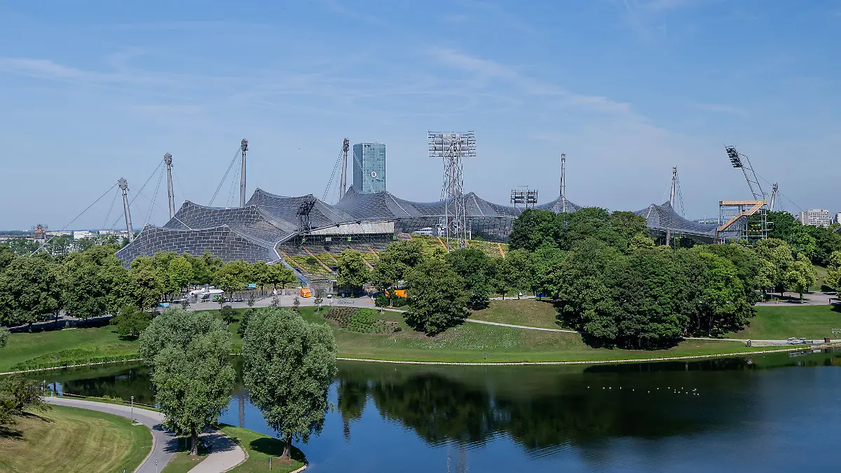 Das-Olympiastadion-mit-der-Zeltdachkonstruktion-hinter-dem-Olympiasee-rechts-im-Bild-der-SAYAQ-Adventure-Tower-ein-Kletterturm-Themenbild-Muenchen-Olympiaparkgelaende-18-06-2026-Foto-HMB-Media-Franz-Feiner-The-Olympic-Stadium-with-its-tent-like-roof-structure-behind-the-Olympic-Lake-on-the-right-side-of-the-photo-is-the-SAYAQ-Adventure-Tower-a-climbing-tower