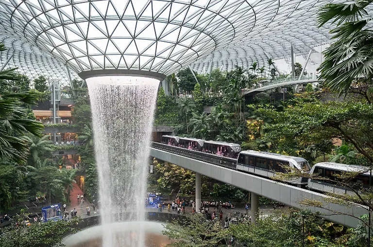 02-10-2025-Singapur-Republik-Singapur-Asien-Zwei-Zuege-der-vollautomatischen-Skytrain-Bahn-durchqueren-den-Innengarten-des-Shiseido-Forest-Valley-mit-dem-Regenstrudel-des-Indoor-Wasserfall-Rain-Vortex-im-Zentrum-des-modernen-Jewel-Terminal-am-Flughafen-Singapur-Changi-Jewel-Changi-ist-ein-Unterhaltungs-und-Einzelhandelskomplex-mit-Naturbezug-der-von-den-Passagierterminals-T1-T2-und-T3-des-Flughafens-Changi-umgeben-und-mit-ihnen-verbunden-ist