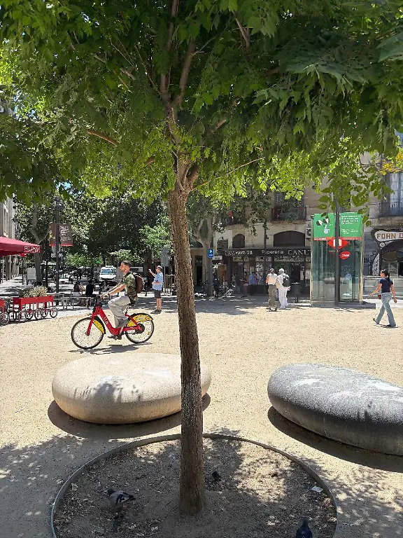 Fussgaenger-und-Fahrradfahrer-auf-der-Kreuzung-der-verkehrsberuhigten-Strassen-Consell-de-Cent-und-Girona-in-Barcelonas-Stadtteil-Eixample-Die-sogenannten-Superilles-aus-mehreren-Haeuserbloecken-inmitten-der-Grossstadt-sind-auch-eine-Antwort-auf-die-immer-groessere-Hitze-in-der-Millionenmetropole