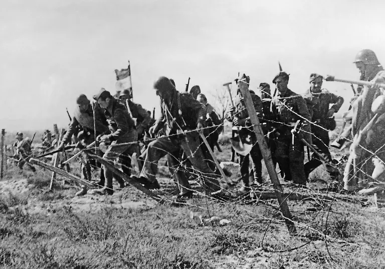 Infanterie-der-nationalspanischen-Fraktion-ueberwinden-im-Sommer-1938-bei-einem-Sturmangriff-an-der-inzwischen-weiter-vorangetriebenen-Teruel-Front-bei-Valencia-durch-niedertreten-einen-republikanischen-Stacheldrahtverhau-Einige-Soldaten-tragen-Pioniergeraet-Hacken-und-Schaufeln-Aufnahmedatum-01-01-1938-31-12