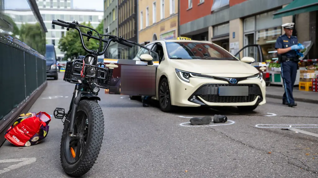 Ein-Polizist-geht-waehrend-seines-Einsatzes-an-einem-Taxi-und-einem-Fahrrad-vorbei-Ein-Taxifahrer-soll-einen-Radler-nach-einem-Streit-in-Muenchen-absichtlich-angefahren-und-schwer-verletzt-haben