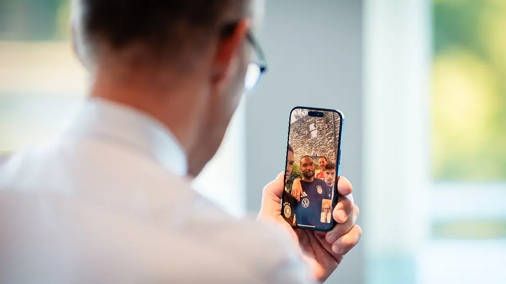 Bundeskanzler-Friedrich-Merz-CDU-spricht-per-Videocall-mit-Spielern-der-Nationalmannschaft-Dabei-ist-Jonathan-Tah-auf-dem-Display-des-Smartphones-zu-sehen