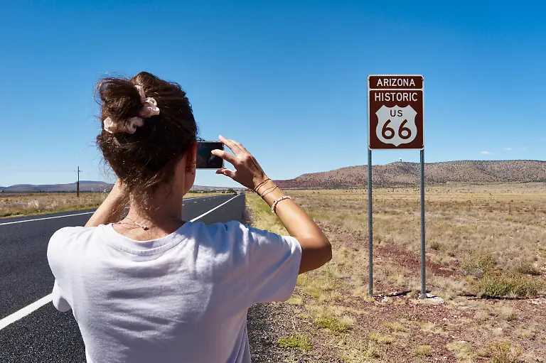 Woman-taking-a-photo-of-Arizona-US-66-road-sign-on-a-sunny-day-in-a-vast-landscape