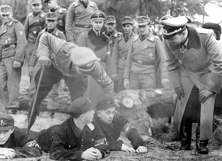 Die-Hitlerjugend-diente-auch-der-vormilitaerischen-Ausbildung-der-Jugendlichen-und-damit-ihrer-Vorbereitung-auf-den-Kriegseinsatz-Hier-wohnen-Offiziere-und-Soldaten-einer-Fronteinheit-der-Wehrmacht-einer-militaerischen-Uebung-von-Hilterjungen-bei-Hintergrund-ist-die-Uebernahme-von-Partnerschaften-zwischen-Hitlerjugend-und-Wehrmachtseinheiten-Der-Offizier-rechts-ist-Eichenlaubtraeger-Oberst-Niemack