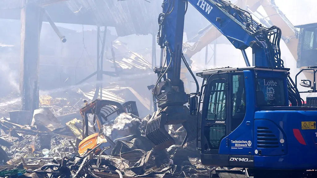 Einsatzkraefte-des-Technischen-Hilfswerks-THW-beseitigen-mit-einem-Bagger-Schutt-nach-einem-Feuer-in-einem-Gewerbegebiet-in-Stuttgart