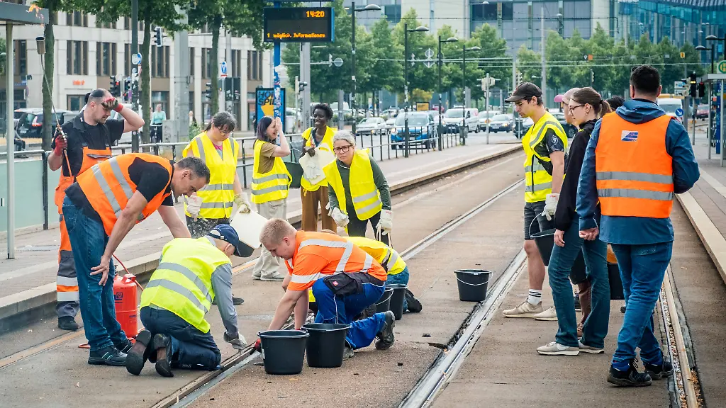 Leipziger-Buergerinnen-und-Buerger-befreien-am-Johannisplatz-gemeinsam-mit-den-Leipziger-Verkehrsbetrieben-LVB-die-Strassenbahngleise-von-geschmolzenem-Bitumen-Nachdem-bereits-am-Vortag-rund-100-Freiwillige-einem-Aufruf-der-LVB-gefolgt-waren-wurden-die-Reinigungsarbeiten-am-zweiten-Tag-am-Johannisplatz-fortgesetzt-Hintergrund-sind-die-Schaeden-durch-die-extremen-Temperaturen-des-vergangenen-Hitzewochenendes-Aufnahme-vom-Datum-Reinigung-Leipzig-Residents-of-Leipzig-together-with-the-Leipzig-Public-Transportation-Authority-LVB-are-clearing-melted-asphalt-from-the-tram-tracks-at-Johannisplatz