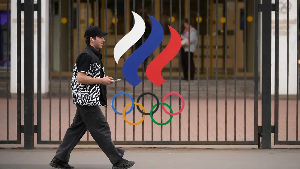 Ein-Mann-geht-vor-dem-Gebaeude-des-Russischen-Nationalen-Olympischen-Komitees-in-der-russischen-Hauptstadt-an-einem-Zaun-mit-den-olympischen-Ringen-vorbei-Das-IOC-hebt-die-Sanktionen-gegen-russische-Sportlerinnen-und-Sportler-vorerst-weitgehend-auf