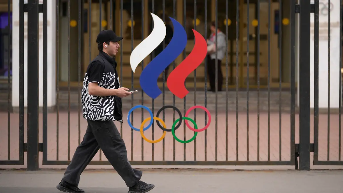 Ein-Mann-geht-vor-dem-Gebaeude-des-Russischen-Nationalen-Olympischen-Komitees-in-der-russischen-Hauptstadt-an-einem-Zaun-mit-den-olympischen-Ringen-vorbei-Das-IOC-hebt-die-Sanktionen-gegen-russische-Sportlerinnen-und-Sportler-vorerst-weitgehend-auf