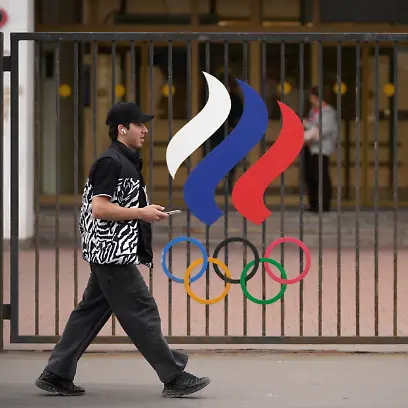Ein-Mann-geht-vor-dem-Gebaeude-des-Russischen-Nationalen-Olympischen-Komitees-in-der-russischen-Hauptstadt-an-einem-Zaun-mit-den-olympischen-Ringen-vorbei-Das-IOC-hebt-die-Sanktionen-gegen-russische-Sportlerinnen-und-Sportler-vorerst-weitgehend-auf