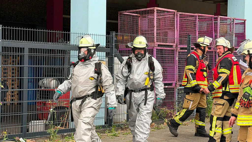 Rettungskraefte-in-Spezialausruestung-sind-an-einer-Lagerhalle-auf-einem-Betriebsgelaende-im-Einsatz