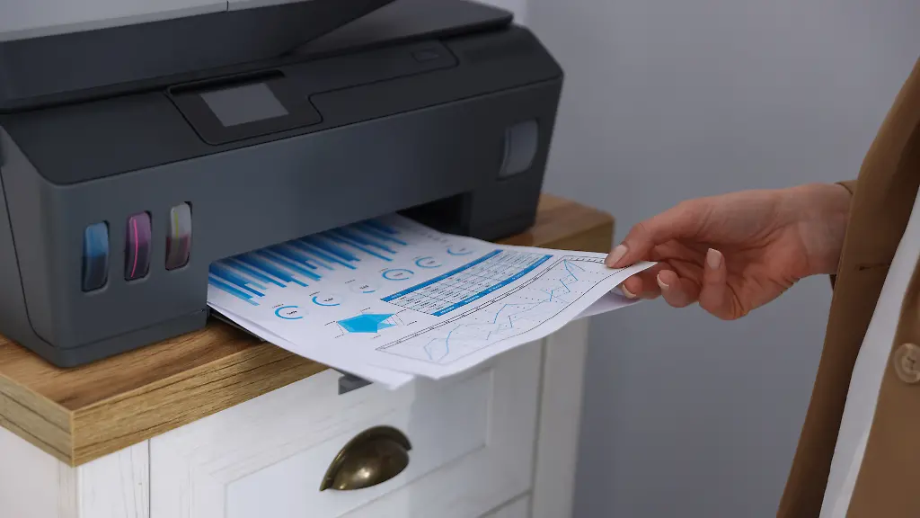 Woman-taking-printed-sheet-of-paper-from-printer-at-chest-of-drawers-indoors-closeup