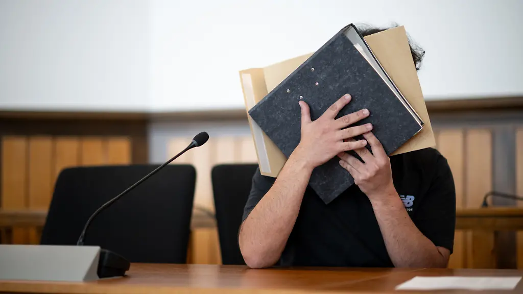 Der-Angeklagte-sitzt-im-Gerichtssaal-und-verdeckt-sein-Gesicht-Er-soll-sich-mit-gefaelschten-Urkunden-eine-Anstellung-als-Notfallsanitaeter-erschlichen-und-Patienten-durch-falsche-Behandlung-in-Gefahr-gebracht-haben-Ein-Patient-ist-gestorben-Die-Anklage-lautet-Totschlag-gefaehrliche-Koerperverletzung-sowie-Urkundenfaelschung