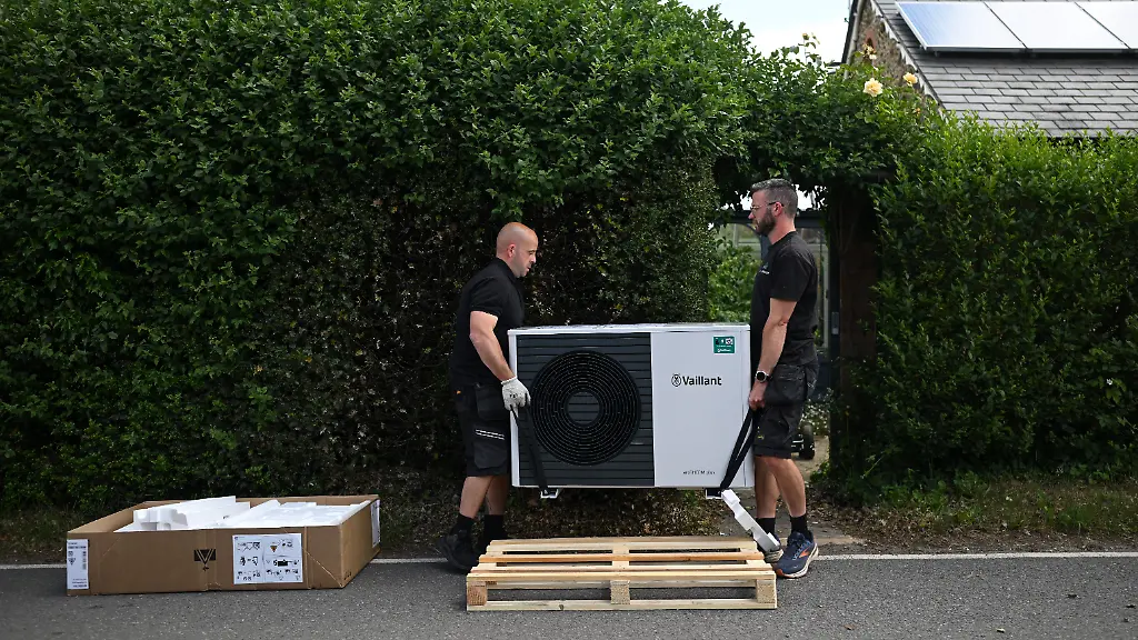 Heat-pump-installers-Simon-Mockler-L-and-Richard-Wilkins-R-from-Lotus-Energy-carry-a-Vaillant-aroTHERM-plus-heat-pump-into-a-residential-property-for-installation-in-Farnham-Surrey-southwest-of-London-on-June-2-2025