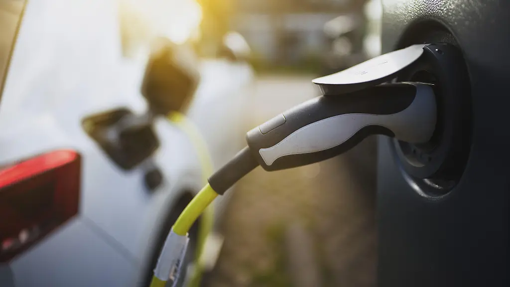 E-Auto-mit-Ladekabel-und-Stromstecker-an-einer-Ladesaeule-angeschlossen-bei-Sonnenaufgang-im-Gegenlicht-in-einem-Wohngebiet-an-der-Strasse-Schagen-Nordholland-Niederlande