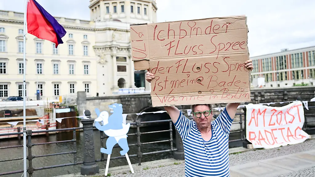 Ein-Mann-steht-waehrend-der-Schwimm-Demonstration-gegen-das-Badeverbot-in-der-Spree-mit-einem-Schild-am-Ufer