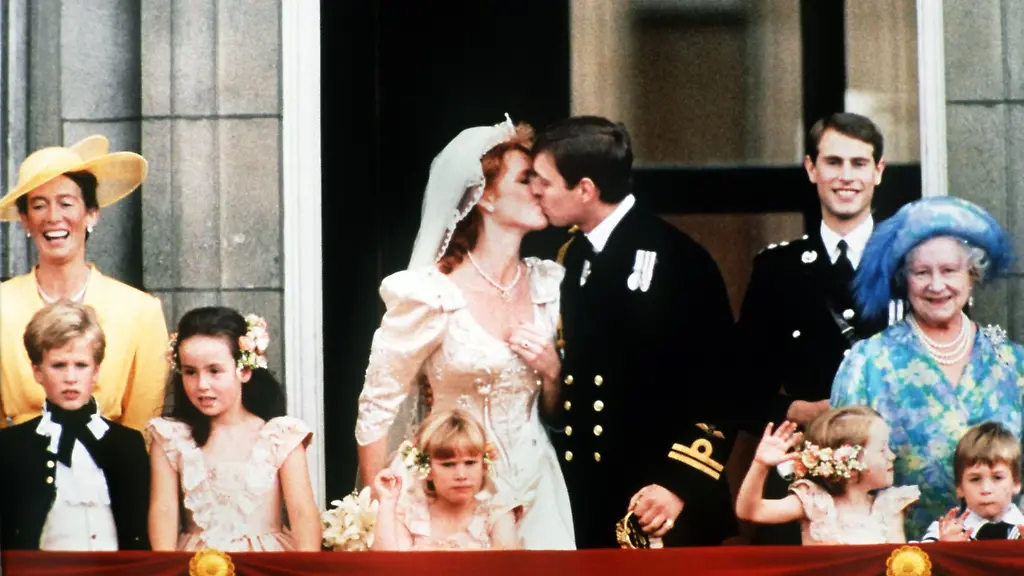 Nach-der-prunkvollen-Hochzeit-am-23-Juli-1986-kuesst-Prinz-Andrew-nach-lautstarken-Aufmunterungen-der-Bevoelkerung-seine-Braut-Sarah-Ferguson-auf-dem-Balkon-des-Londoner-Buckingham-Palastes-Rechts-freut-sich-Koeniginmutter-Elizabeth-dahinter-der-Bruder-des-Braeutigams-Prinz-Edward