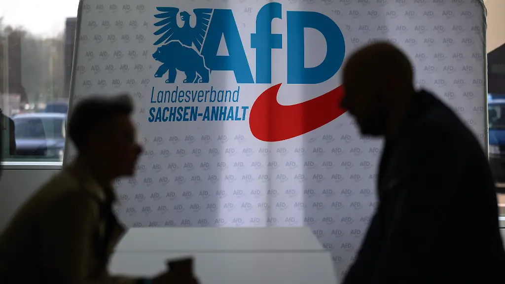 Teilnehmer-des-Landesparteitages-der-AfD-Sachsen-Anhalt-in-Magdeburg-unterhalten-sich-vor-einer-Wand-mit-dem-Parteilogo-Die-Delegierten-des-Landesparteitages-wollen-das-Regierungsprogramm-zur-Landtagswahl-2026-final-erarbeiten-und-beschliessen