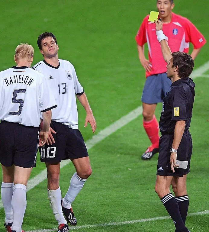 Der-Schweizer-Schiedsrichter-Urs-Meier-r-vorn-zeigt-dem-deutschen-Mittelfeldspieler-Michael-Ballack-2-v-l-die-Gelbe-Karte-An-Ballacks-Seite-Carsten-Ramelow-l-Die-deutsche-Fussballnationalmannschaft-gewinnt-am-25-06-2002-in-Seoul-das-Halbfinalspiel-des-17-WM-Turniers-gegen-die-Elf-des-Gastgebers-Suedkorea-durch-Ballacks-Tor-mit-1-0-und-qualifiziert-sich-damit-zum-siebentenmal-fuer-das-Endspiel-in-dem-Ballack-nach-seiner-zweiten-Gelben-Karte-fehlt