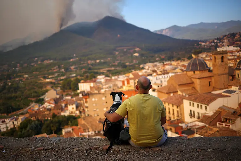 A-man-and-his-dog-look-at-a-wildfire-in-a-mountain-in-Onda-Spain-July-27-2026